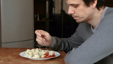 Adam onları Mutfakta domates sosu içine koyarak bir çatalla köfte yiyor.