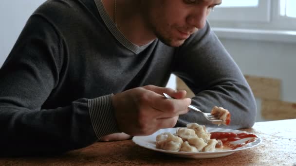 Man eats dumplings with a fork, putting them into tomato sauce in the kitchen — Stock Video