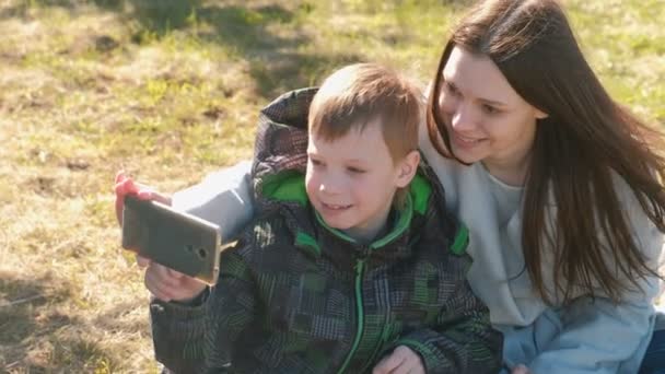 Moeder en zoon maken selfie op mobiele telefoon in voorjaar park. — Stockvideo