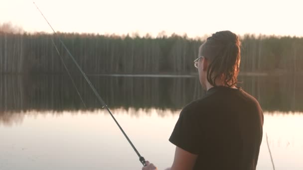 Rybak na stawie. Młody facet z dredy w okularach w ryby wędkarstwo t-shirt z prętem. — Wideo stockowe