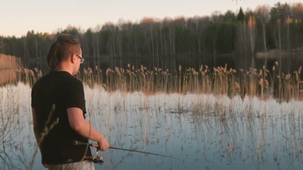 Rybak na stawie. Młody facet z dredy w okularach w ryby wędkarstwo t-shirt z prętem. — Wideo stockowe