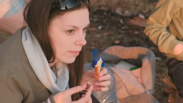 Junge brünette Frau, die Brot und Fleisch auf Feuer gebraten isst. Campingausflug. — Stockvideo