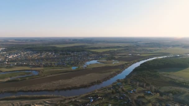 Flight above green fields, forest, river and village early spring, aerial panoramic view. — Stock Video
