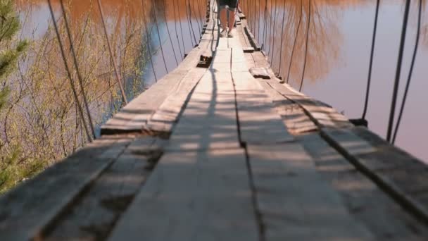 Крупным планом ноги семьи мама, папа и дочь идут по старому подвесному мосту через реку . — стоковое видео