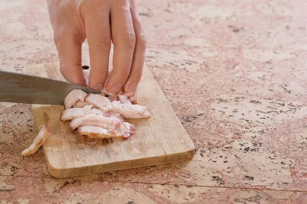 Человек режет свиную грудинку беконом на мелкие кусочки на деревянной доске. Рука крупного плана . — стоковое фото