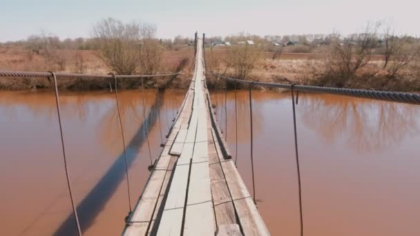 L'uomo sta camminando su un ponte sospeso di legno sul fiume. Vista in prima persona . — Video Stock