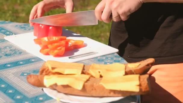 O jovem corta pimenta vermelha no tabuleiro. Preparação de sanduíches. Mãos fechadas . — Vídeo de Stock