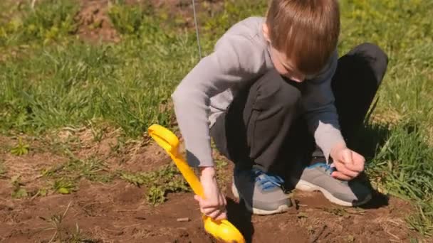 Хлопчик копає землю жовтою пластиковою лопатою на газоні біля будинку . — стокове відео