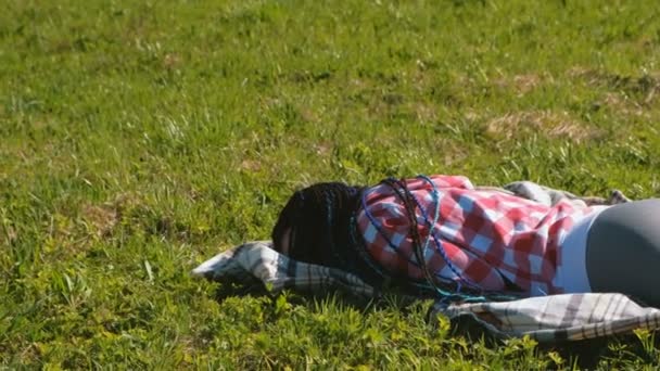 Mujer irreconocible con trenzas africanas azules durmiendo en el césped del parque . — Vídeo de stock