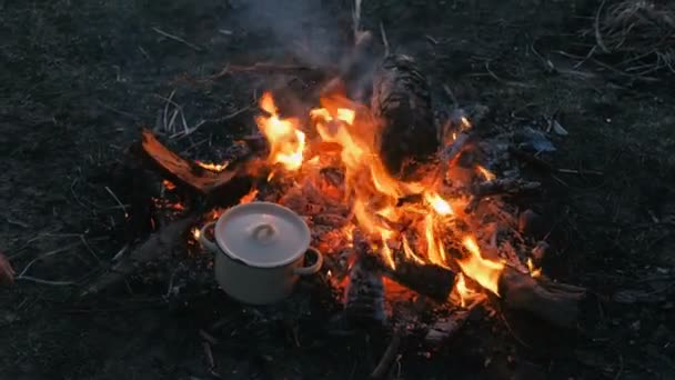 Il cibo viene cotto sul falò in una pentola. Le mani delle donne toccano con il piatto . — Video Stock