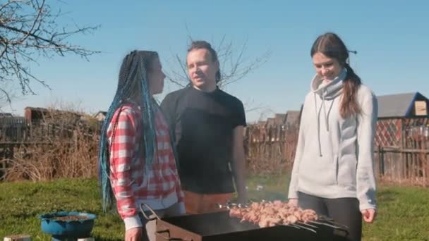 Grupo de jovens amigos Churrasco shashlik carne em cima da grelha de carvão no quintal. Conversando e sorrindo juntos . — Vídeo de Stock