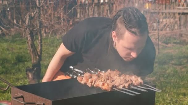 Joven con rastas en los pelos cocina carne shashlik en la parte superior de la parrilla de carbón en el patio trasero . — Vídeos de Stock