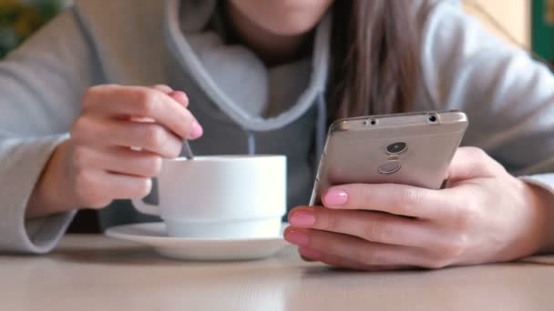 Femme boit un chocolat chaud avec cuillère et regarder sur l'écran de téléphone portable assis dans le café. Gros plan womans mains .