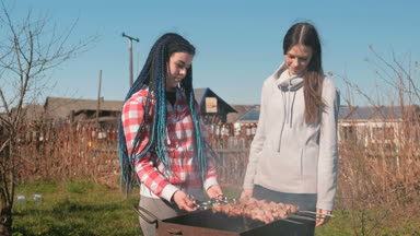 İki kadın arkadaş üstünde tepe-in arka bahçesinde üzerinde kömür ızgara Kebab et pişirmek. Konuşmak ve birlikte gülümseyen.