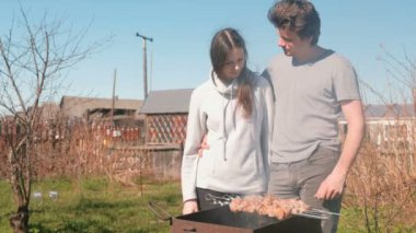 Çift erkek ve kadın üstüne arka bahçesinde üzerinde kömür ızgara Kebab et pişirmek. Konuşmak ve birlikte gülümseyen.