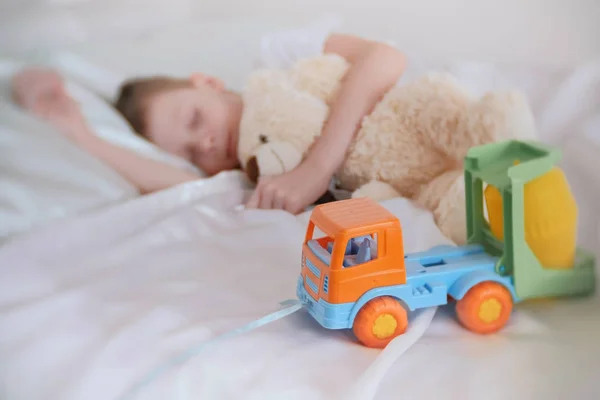 Menino de sete anos dormindo com seus brinquedos urso e carro de plástico. Foco em carro de brinquedo . — Fotografia de Stock
