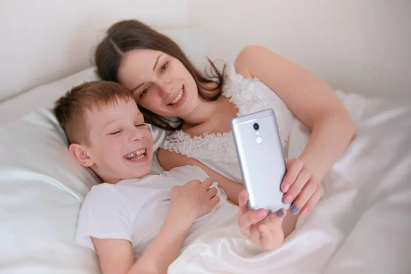 Mom and son take selfie on her mobile phone. Morning in bed.