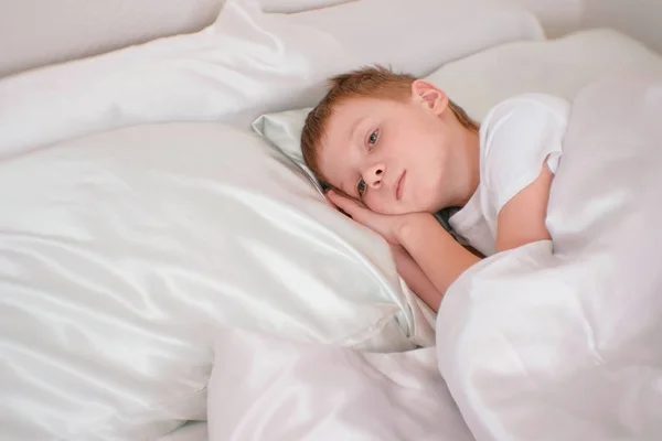 Menino de sete anos acorda em sua cama debaixo do cobertor — Fotografia de Stock