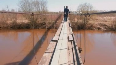 Baba ve oğlu eski asma köprü Nehri üzerinde yürümek. Arkadan görünüm.