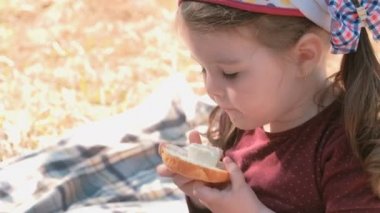 Küçük şirin kız ekmek ile sandviç yiyor ve peynir işlenebilir. Aile pikniği. Pis parmaklarını yalıyor.