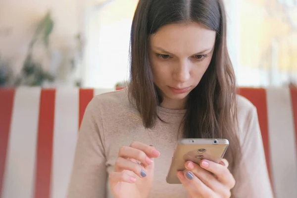 Junge schöne Frau brünett surft im Internet in ihrem Handy im Café und wartet auf ihre Freunde — Stockfoto
