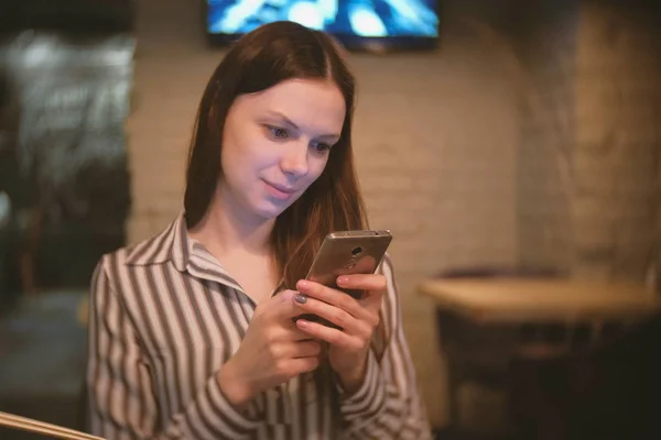 Kvinnen leser Internett på mobilen og ser inn i kamera og smiler. . – stockfoto