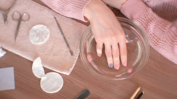 Manicura en casa. Mujer sumergiendo su mano en un tazón de agua. Primer plano de la mano, herramientas de manicura sobre la mesa. Vista superior . — Vídeo de stock