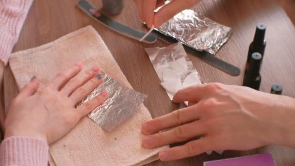 Removing gel Polish from nails. Man pours remove liquid on a cotton pad, puts it on a womans nail and wraps the foil. Close-up hands. — Stock Video