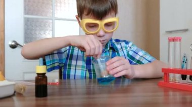 Evde kimya üzerinde deneyler. Oğlan mavi sıvı ve toz kabı içinde cam sopa ile karışımları.