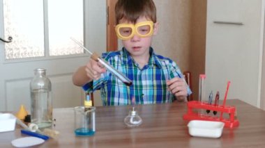 Evde kimya üzerinde deneyler. Çocuk tüp üzerinde alkol lamba yanan kırmızı sıvı ile ısıtır.