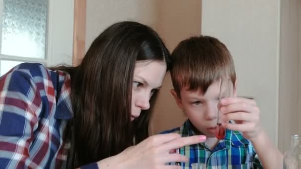 Chemické pokusy doma. Máma a syn dělají experiment s červenou barvou a vody. — Stock video