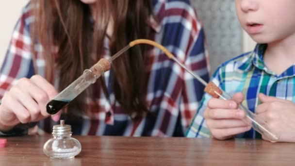 室内化学实验。男孩和他妈妈用蓝色液体在燃烧酒精灯上加热试管. — 图库视频影像