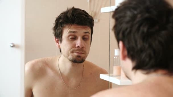 Müder Mann, der gerade aufgewacht ist, blickt auf sein Spiegelbild im Spiegel und überrascht. — Stockvideo