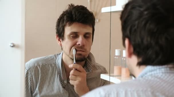 Hombre cansado y somnoliento con resaca que acaba de despertar cepillarse los dientes, mira su reflejo en el espejo . — Vídeo de stock