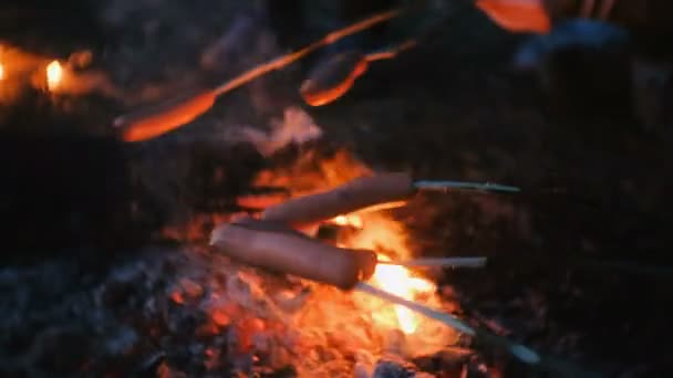 La gente frigge salsicce su un fuoco nel bosco di notte. Salsicce da primo piano . — Video Stock