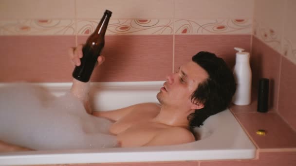 Joven toma un baño con espuma y bebe cerveza . — Vídeo de stock