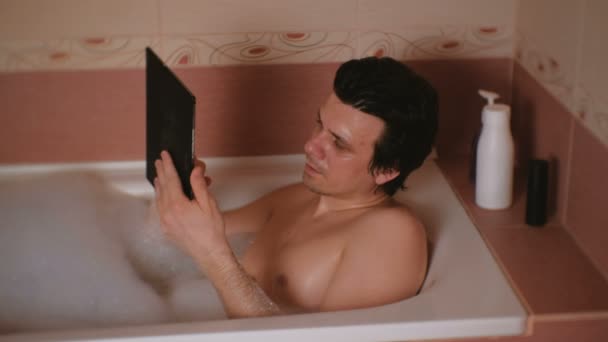 Młody człowiek bierze kąpiel, pisania wiadomości na tablet. — Wideo stockowe
