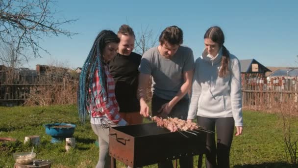 Groep jongeren vrienden Barbecue sjasliek vlees bovenop de houtskool barbecue op achtertuin. Praten en lachen samen. — Stockvideo