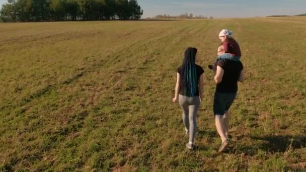 Familiedag af. Moeder, vader en dochter lopen op het eindeloze veld. Mooie zomerse landschap. Achteraanzicht. — Stockvideo