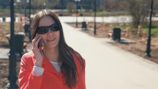 Jeune femme brune en lunettes de soleil parle au téléphone au printemps Park . — Video