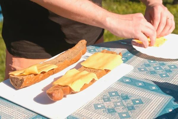 Mann macht Sandwiches mit Brot und Käse auf einem Picknick. Hände aus nächster Nähe. — Stockfoto