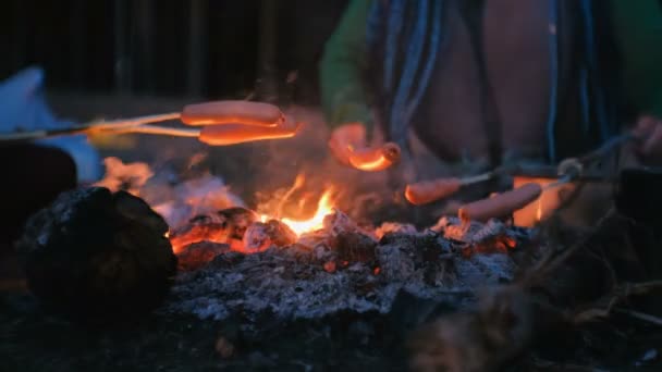 La gente frigge salsicce su un fuoco nel bosco di notte. Mani in primo piano . — Video Stock