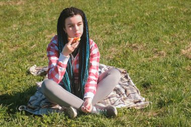 Genç kadın esmer içinde park piknik sandviç yiyor.