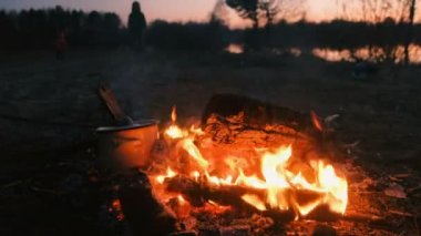 Gıda kapak şube ile bir tavada, açık ateş üzerinde pişirilir. Nehir kıyısındaki kamp içinde insanlar.