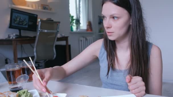 Jonge vrouw brunette eet rollen met houten stokken thuis. — Stockvideo