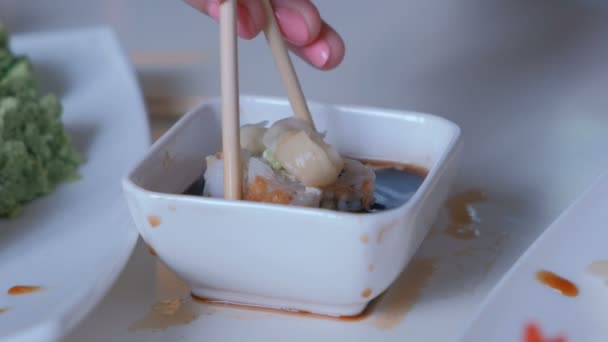 Kobieta zjada roll. Stawia roll w sosie sojowym, ucząc się jeść z patyków. Bliska. — Wideo stockowe