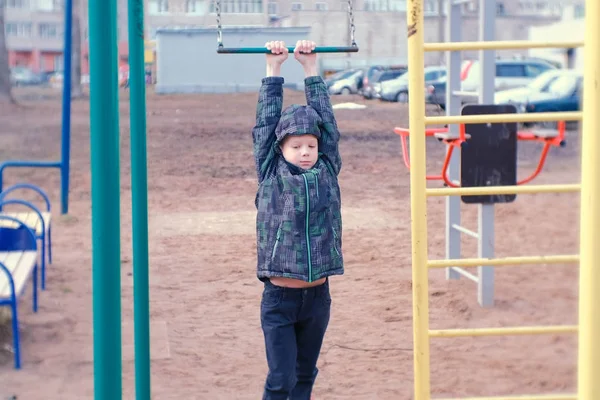 Мальчик качается на гимнастическом трапеции, прыгает и падает на песок. Детская площадка во дворе городского дома . — стоковое фото