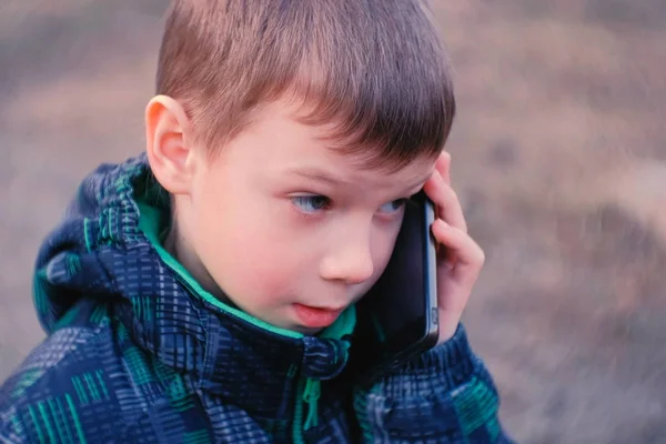 Мальчик говорит по мобильному телефону в парке и смеется. Вид спереди, лицо крупным планом . — стоковое фото