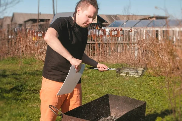 Genç adam bir kesme tahtası ile ızgara mangal kömürleri açılırsa.