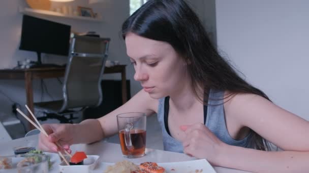 Νεαρή γυναίκα μελαχρινή τρώει ρολά με ξύλινα ραβδιά στο σπίτι. — Αρχείο Βίντεο